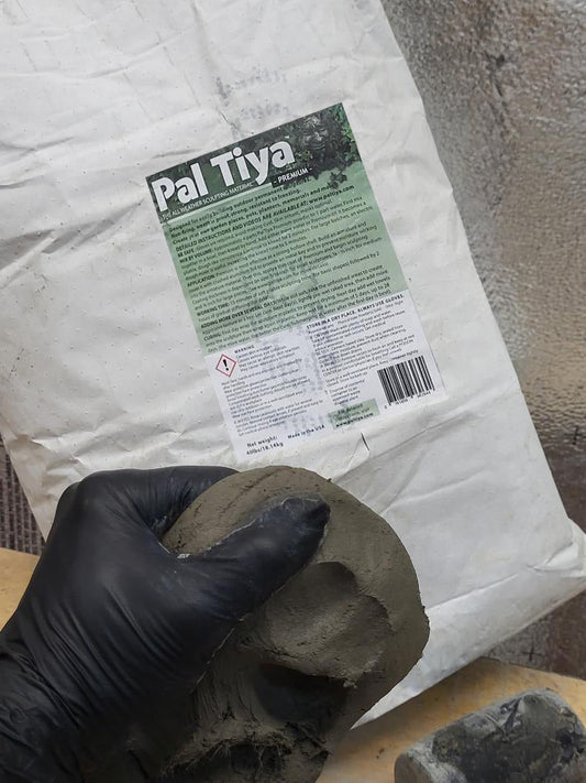 A gloved hand holding a piece of worked Pal Tiya Premium fortified cement sculpting material in front of a 40 lb Pal Tiya Premium bag